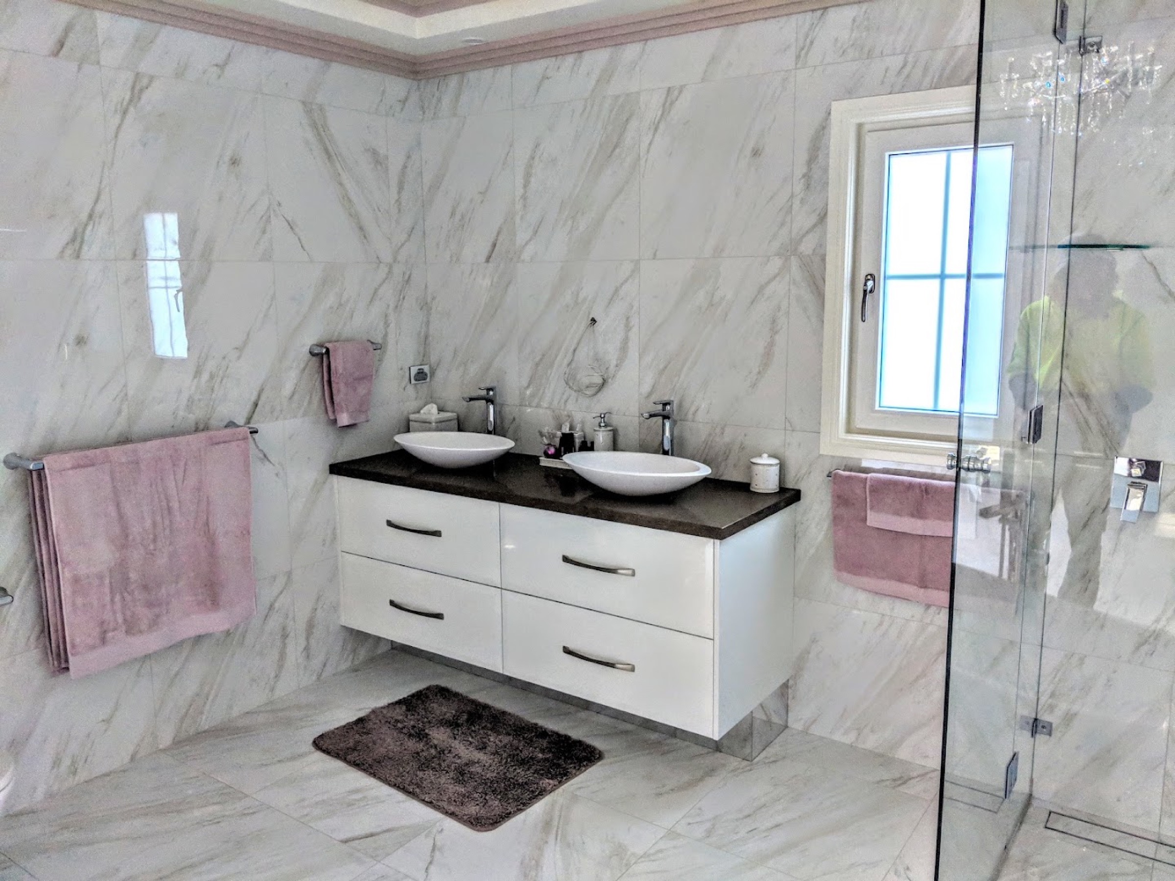 A modern bathroom with large-format tiles, a glass shower screen and marble vanity