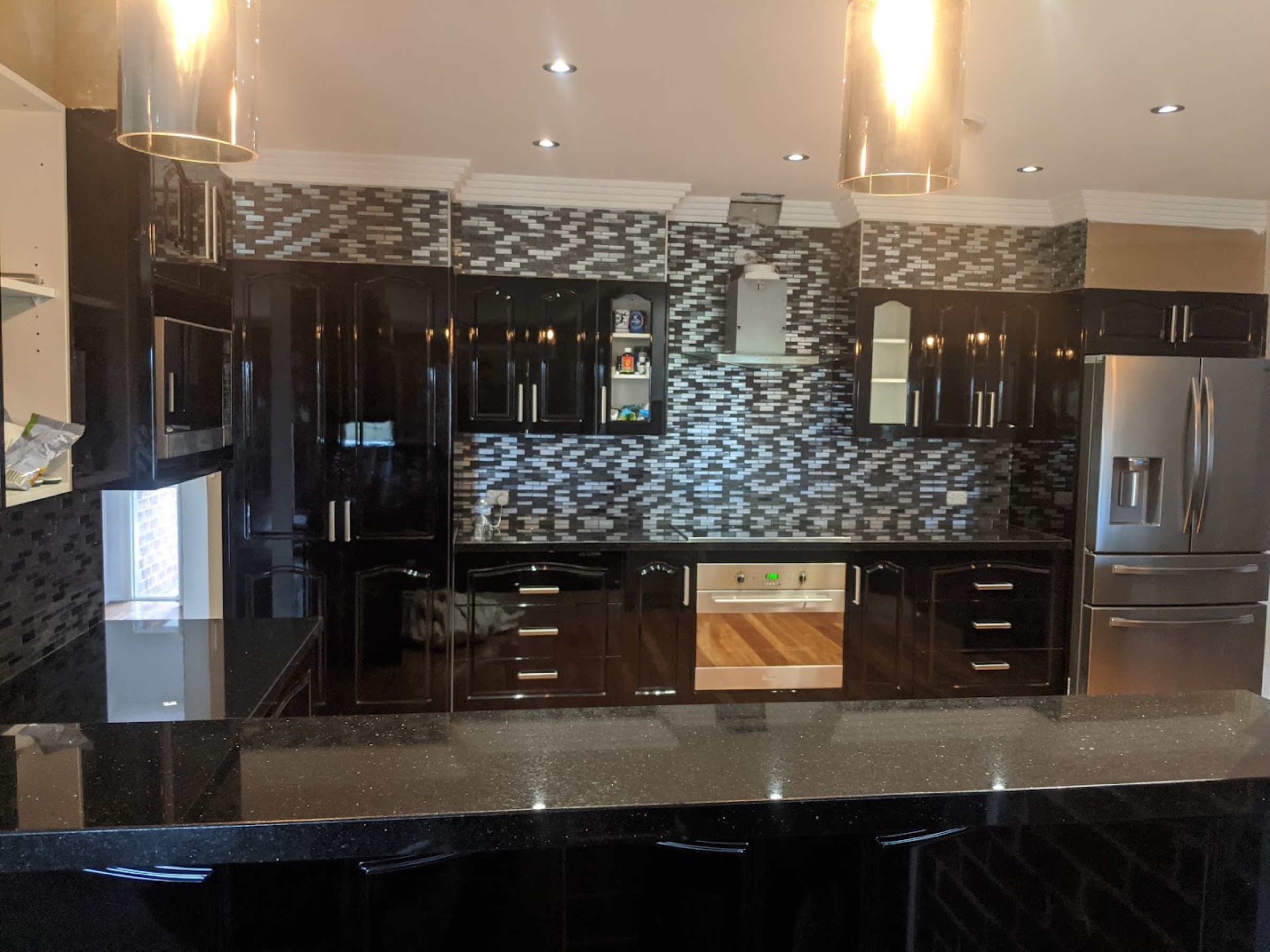 A dark kitchen with a herringbone tile splashback and brass tapware
