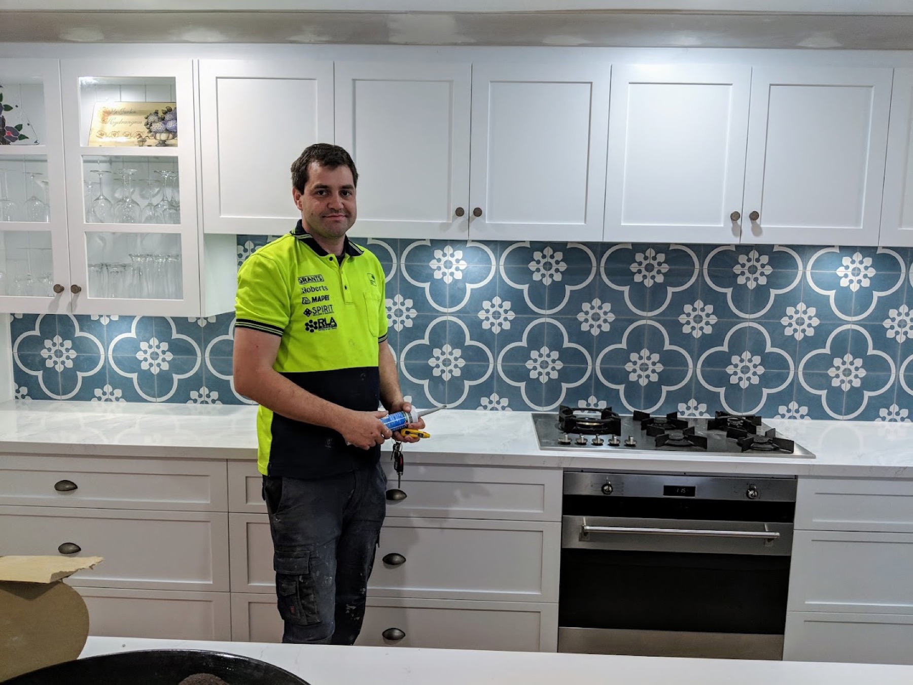 A tradesperson in hi-vis workwear standing in front of a finished patterned kitchen splashback