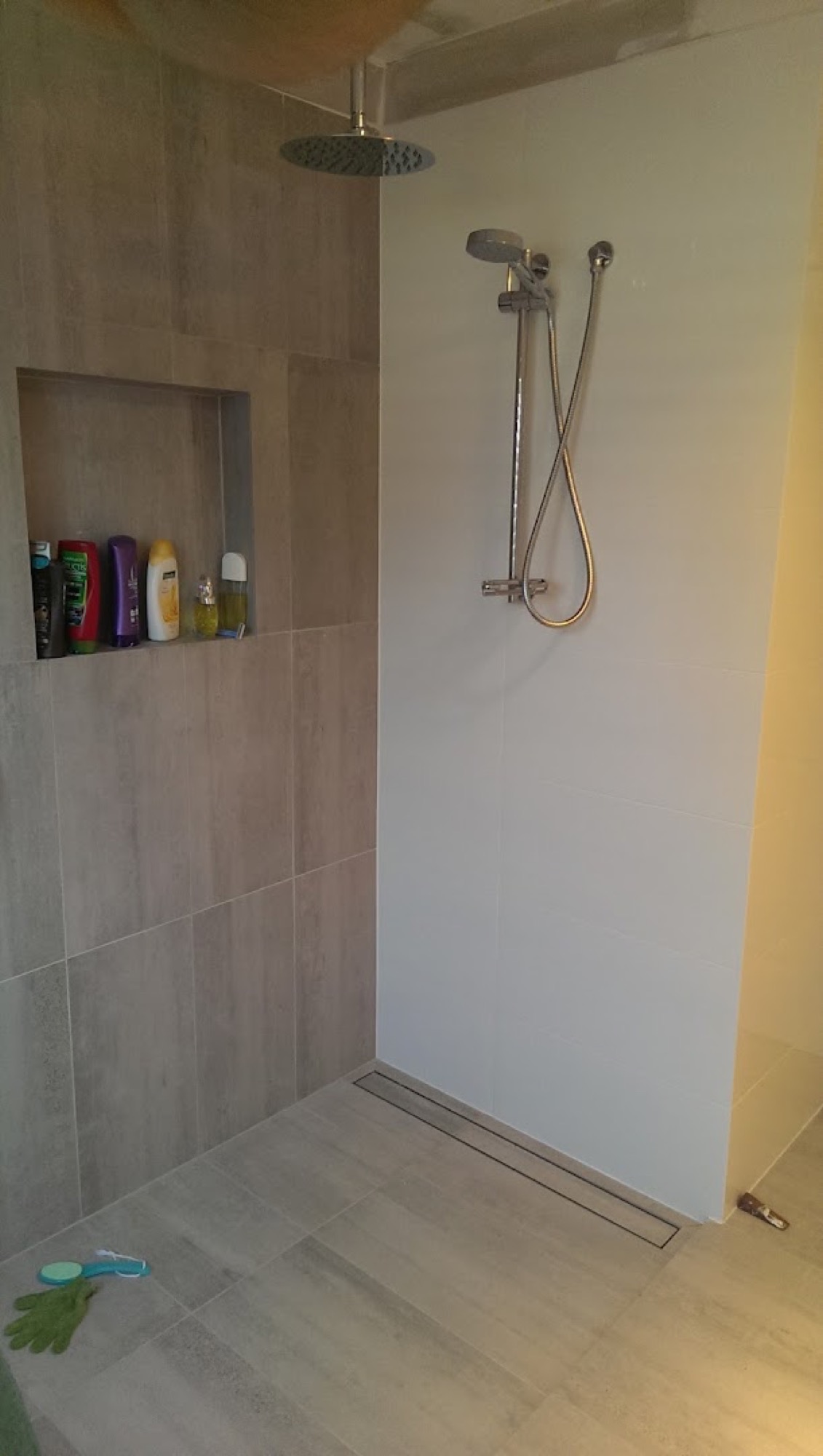 A tiled shower recess with a rain shower head and toiletries on a shelf