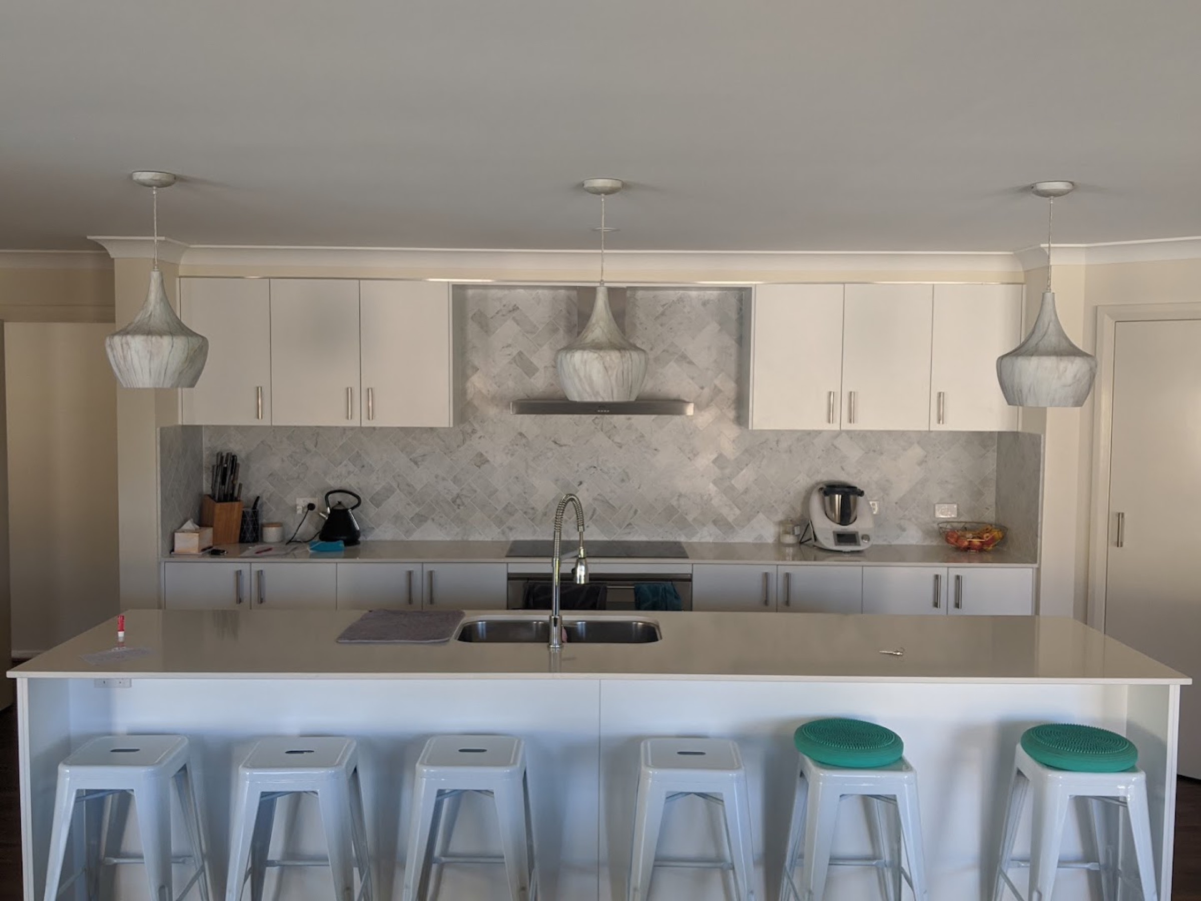 A white kitchen with a marble island bench and tiled floor