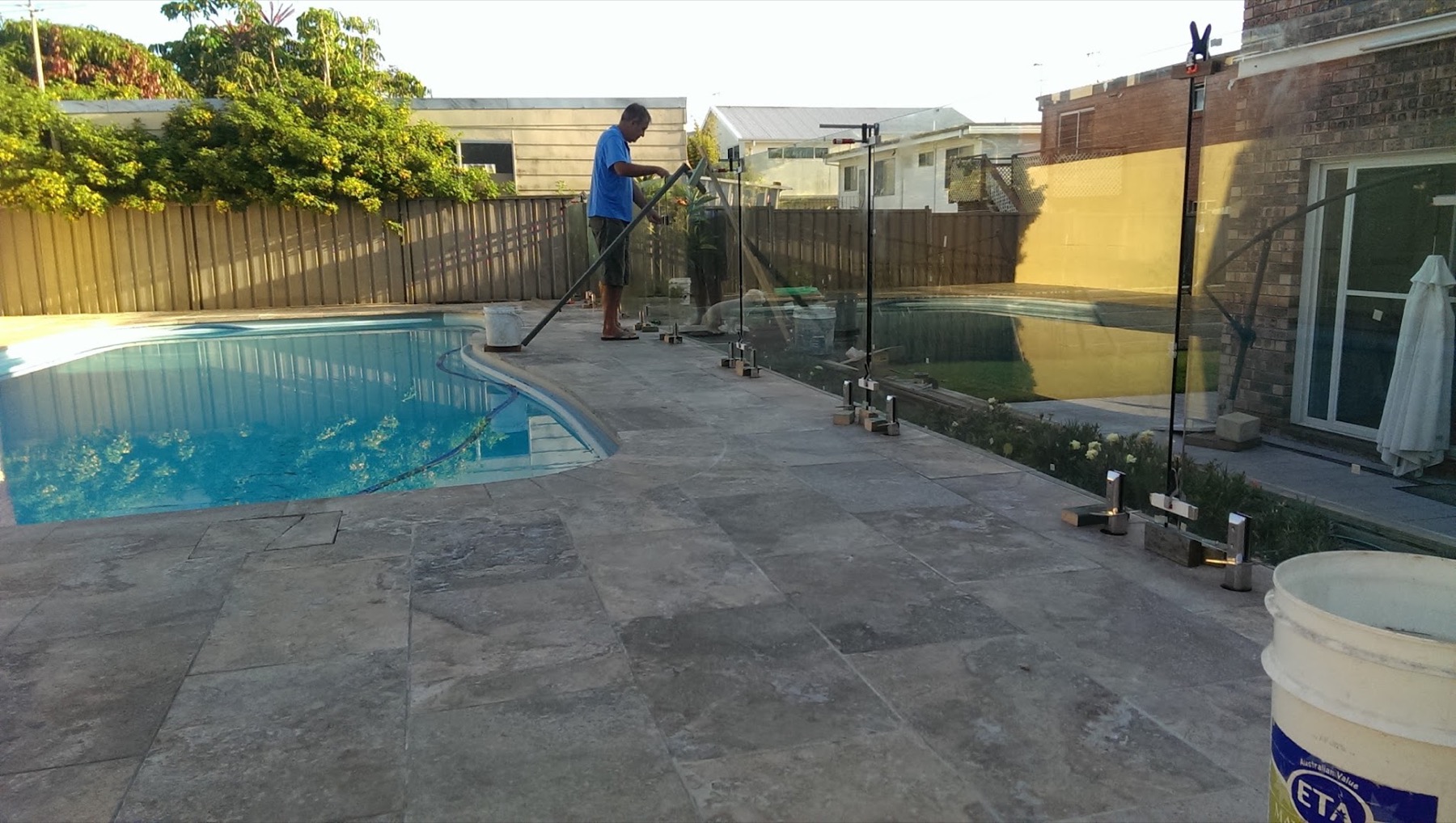 A tradesperson standing beside a glass pool fence next to travertine paving