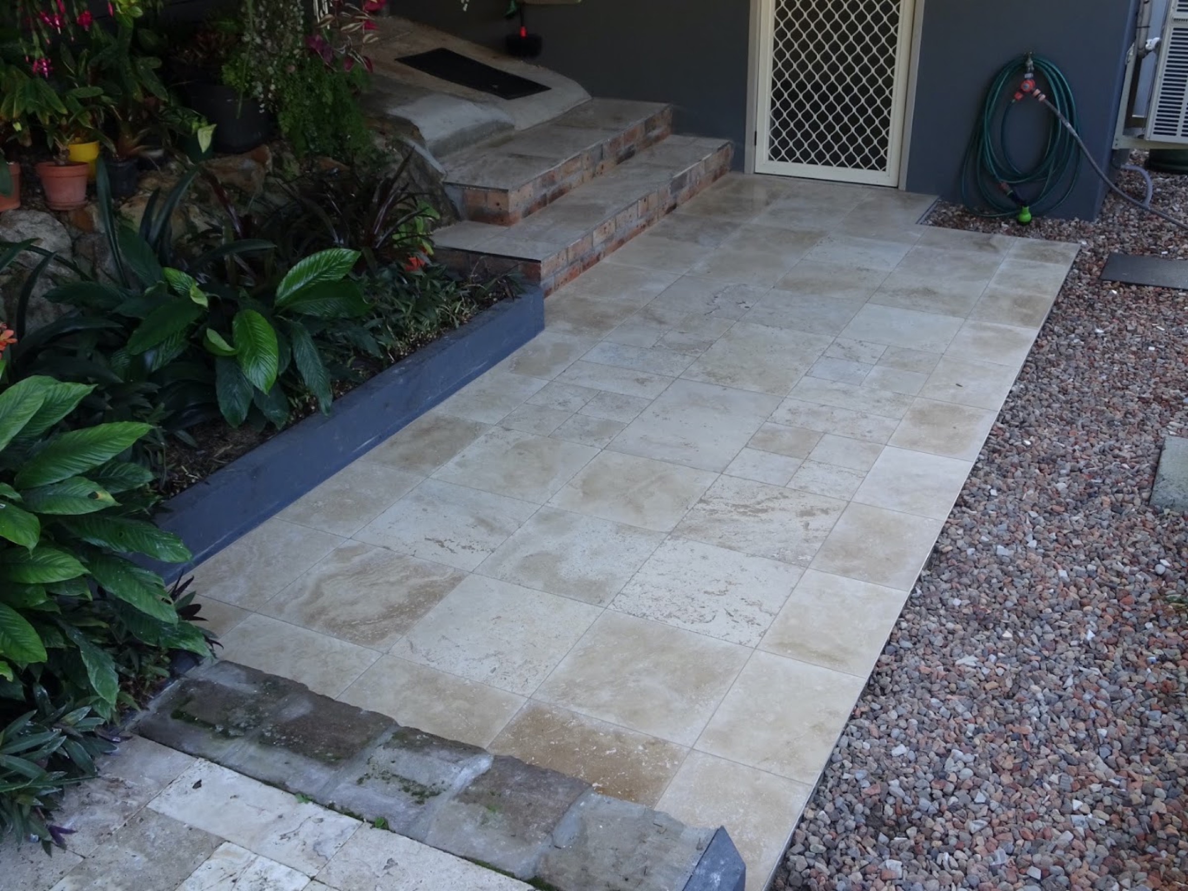 Travertine garden steps and paving beside a glass pool fence