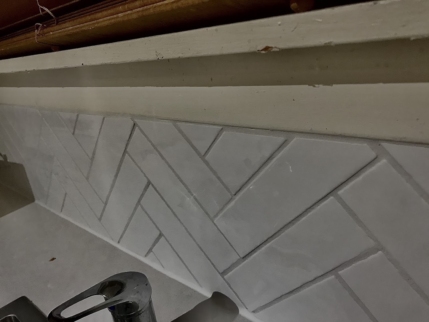 A herringbone pattern tile splashback under a timber kitchen shelf