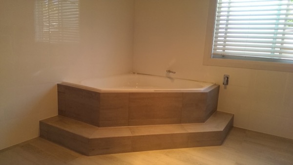A tiled corner bathtub with a tiled step in front of a window