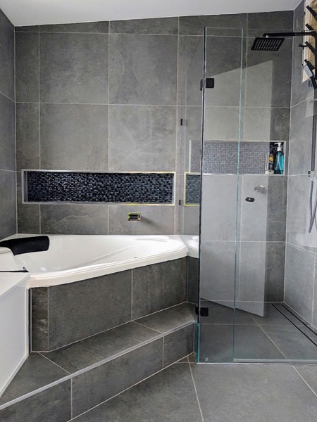 A tiled bath surround with a mosaic tile inset border