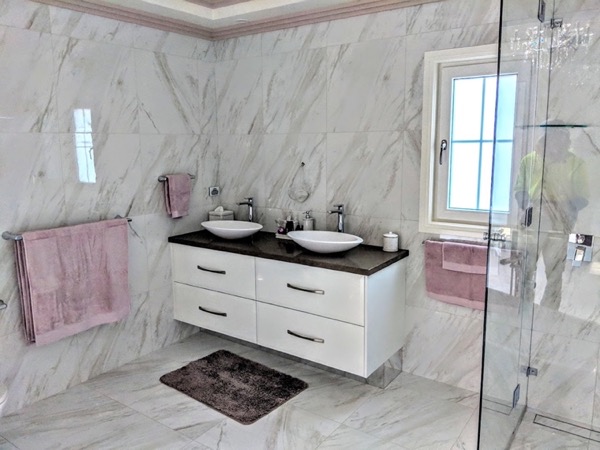A bathroom with large marble-look tiles, a glass shower screen and floating vanity