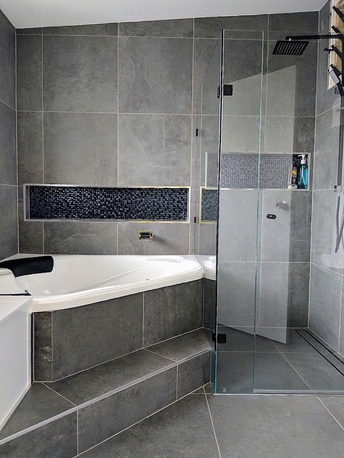 A tiled corner bath surround with a mosaic tile inset
